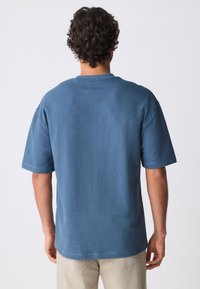 T-shirt blu a maniche corte con collo rotondo, realizzato in tessuto morbido. Presenta una vestibilità rilassata e dettagli di cuciture sottili lungo i bordi.