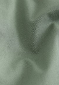 Tissu lisse vert clair avec un fin motif de tissage diagonal et des plis doux créant des ombres et de la texture.