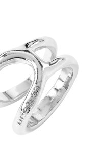 Anillo de plata con un diseño retorcido, superficies lisas y pulidas, y una ligera calidad reflectante. Marca grabada en la parte interior de la banda.