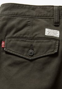 Tkanina bawełniana w oliwkowym kolorze typu twill z kieszenią na plecach w kształcie diamentu, z czarnym guzikiem i białą metką marki Levi's.