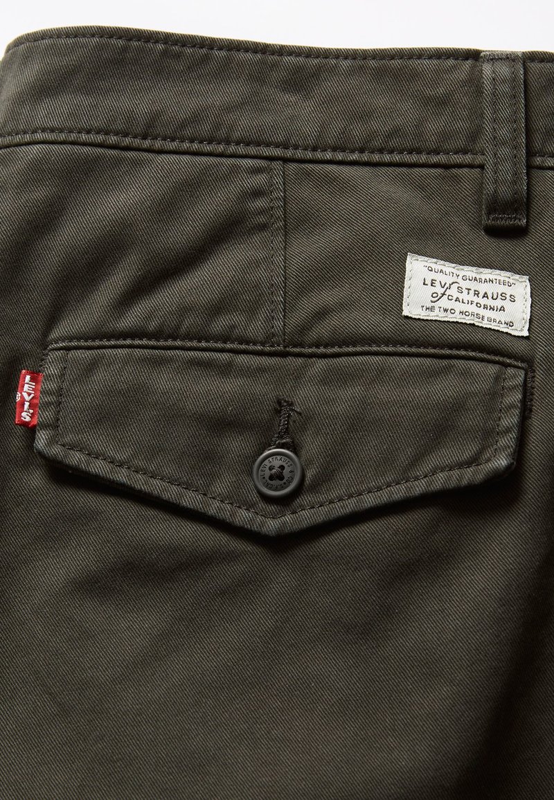 Tela de sarga de algodón verde olivo con un bolsillo trasero en forma de diamante, que cuenta con un botón negro y una etiqueta de marca Levi's en blanco.
