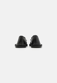 Svarte skinsko med avrundede bakker, dekorativ søm på sidene og teksturerte såler. Rent design og minimale hardware-detaljer.