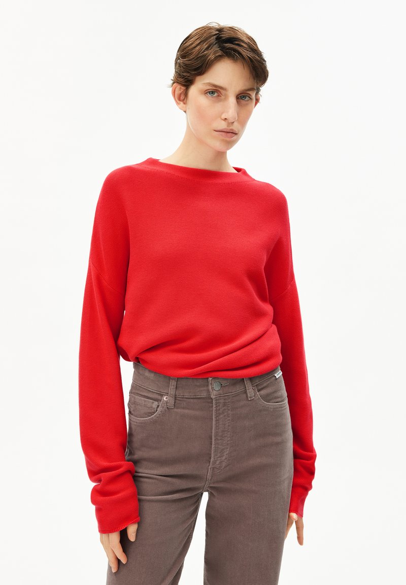 Rode, geribde trui met een bootnek en lange mouwen, gecombineerd met bruine corduroy broek met hoge taille en voorzakken.