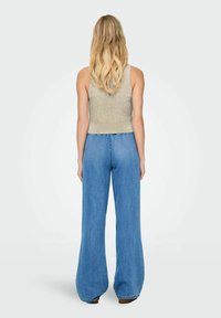 Beige geribbelde tanktop met een cropped ontwerp, gecombineerd met lichtblauwe, high-waisted flare jeans met een middennaad op de achterkant.