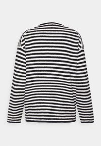 Raidallinen neulepaita pehmeästä, pörröisestä kankaasta, jossa on vaakasuorat mustavalkoiset raidat, pyöreä pääntie ja pitkät hihat, joissa roikkuvat olkapäät.