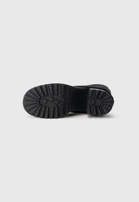 Black boot sole with deep tread pattern, textured surfaces, and prominent lugs for grip. Material appears sturdy and durable.