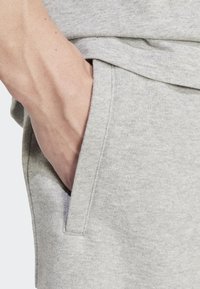 Light gray cotton sweatpants with a side pocket and a soft, textured fabric. Close-up view of a hand resting in the pocket.
