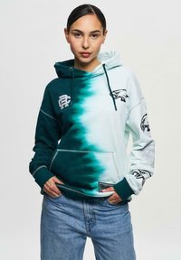 Huvtröja med en övergång från mörk teal till ljusgrön. Har logotyper, framficka och ribbad mudd. Tillverkad av mjukt tyg.