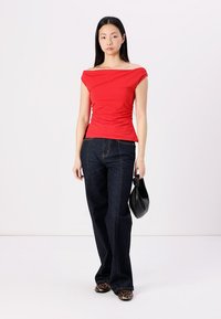Red off-the-shoulder top with gathered texture, paired with dark blue straight-leg jeans. Accessories include a black handbag and leopard-print shoes.