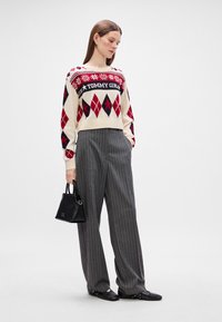 Krém színű pulóver piros és tengerészkék argyle mintával, valamint "TOMMY GIRL" felirattal, szürke csíkozott, bő szárú nadrággal és egy kis fekete kézitáskával párosítva.