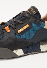 Tmavě šedé a modré tenisky z textilního a koženého materiálu, s oranžovými akcenty, texturovanou podešví a brandingem "REPLAY" na boku.