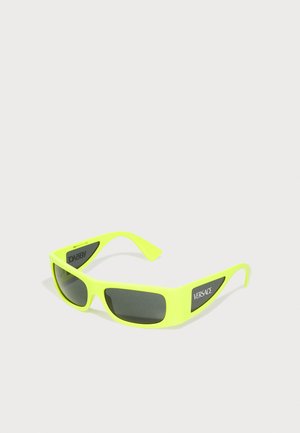 Occhiali da sole giallo neon con lenti grigie. Presentano una robusta montatura in plastica e accenti del logo Versace su materiale nero alle tempie.