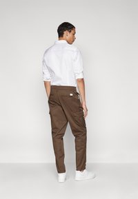 Brown cargo pants with side pockets, a straight cut, and a label at the back, paired with a white button-up shirt and white sneakers.