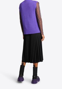 Lila gerippter ärmelloser Top, schwarzer plissierter Rock und schwarze Stiefel mit lila Sohlen, mit einer strukturierten Überlagerung an den Ärmeln.