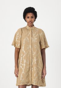 Abito beige a maniche corte con colletto alto, caratterizzato da un motivo a catena argentata, tessuto leggero e una linea morbida e fluida.