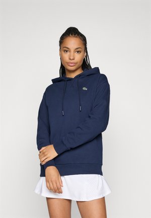 Marinblå hettegenser laget av mykt materiale, med en front kangaroo-lomme og en liten brodert logo på brystet.