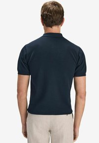Marinblå kortärmad polotröja med en strukturerad stickad mönster, med en klassisk krage och en rak passform, sett bakifrån.