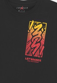 Camiseta de algodón negra con un audaz diseño gráfico en amarillo y rojo, que muestra "¡BAILEMOS!" y un motivo dinámico parecido a un rayo.