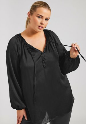 Blusa negra con mangas largas y vaporosas, tela texturizada, escote en V y una fila de botones en el frente. Hay lazos en el cuello.