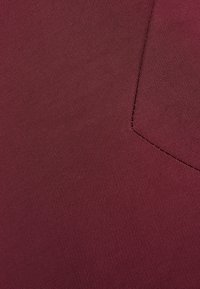 Burgundská látka s jemnou, hladkou texturou. Obsahuje šitý šev a detail kapsy, zobrazuje rovnoměrné zbarvení po celém povrchu.