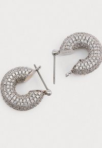 Sølvringe i spiraldesign, dækket med klare krystaller, med en blank finish og en pin-back. Den teksturerede overflade reflekterer lyset.