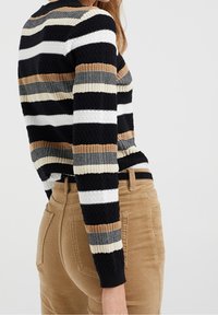 Stickad tröja med svarta, vita, beige och bruna horisontella ränder. Har ribbade ärmslut, strukturerad tyg och en figurnära design.