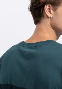 Teal T-shirt met korte mouwen en een ronde halslijn, met subtiele logo-details nabij de achterkant van de nek. Zachte stof en een relaxte pasvorm.