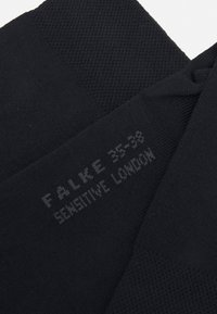 Calze nere Falke con un design lavorato a maglia testurizzato. Presentano una taglia e il nome del marchio stampati: "FALKE 35-38 SENSITIVE LONDON" in grigio sottile.