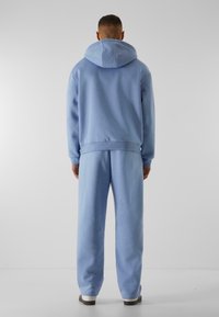Lysblå hoodie og sweatpants sæt, der har en stor hætte og ribbede manchetter. Materialet ser blødt ud med en glat tekstur.