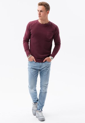 Burgundy långärmad skjorta med bröstficka, kombinerad med ljusblå slitna jeans och grå sneakers, som skapar en avslappnad outfit.