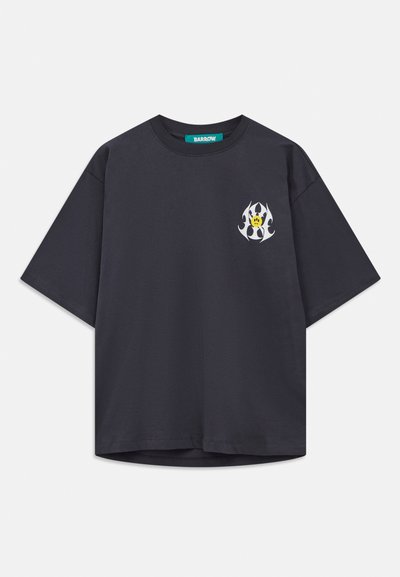 Black oversized t-shirt with round neck and small white flame design featuring a yellow smiley face on the left chest, branded neck label.