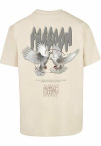 Cremefarvet bomulds t-shirt med grafik af to hvide duer og ordet "FREEDOM" i grå skrift over ryggen.