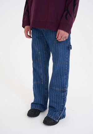 Niebieskie dżinsowe spodnie w paski o luźnym kroju, z kieszeniami z przodu i wzmocnionymi szwami, w zestawieniu z czarnymi, teksturowanymi butami.