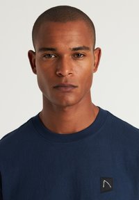 T-shirt in cotone blu navy con collo rotondo e un piccolo patch con logo ricamato sul lato sinistro del petto. Tessuto liscio, maniche corte.
