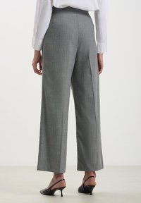 Pantaloni grigi a vita alta con motivo a righe, dal taglio dritto e gambe svasate. Indossati con mule nere con tacco.