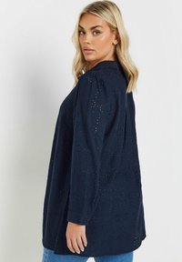Camicia a maniche lunghe blu navy con motivo floreale a occhio di persiana, polsini con bottone, vestibilità comoda e dettaglio con piega sul retro. Il tessuto testurizzato aggiunge dimensione.