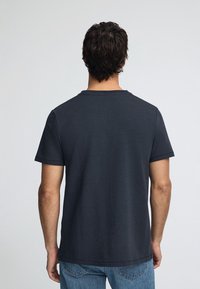 Camiseta de manga corta gris oscuro, diseño de cuello redondo, hecha de una tela suave, presenta una textura lisa con dobladillos cosidos.