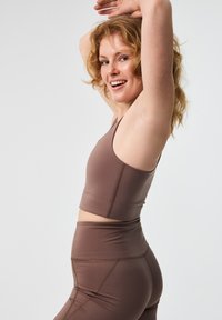 Barna sportmelltartó és passzoló, magas derekú leggings, rugalmas anyagból készült, kontrasztos varrással és testes kialakítással.