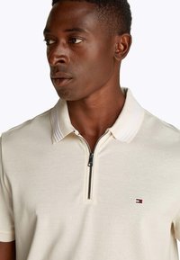 Polo da uomo color crema con collo a zip, tessuto strutturato e collo a righe. Presenta un piccolo logo sul petto.