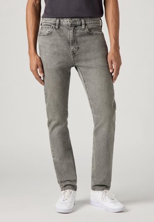 Jeans in denim grigio con vestibilità dritta, cuciture dettagliate, cinque tasche e chiusura con bottoni, abbinati a sneakers bianche.