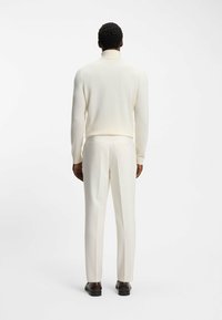Witte gebreide coltrui gecombineerd met op maat gemaakte witte broeken, met een gladde textuur en strakke lijnen, gedragen met donkere schoenen.