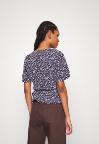 Marineblå blomstret topp med korte ermer, samlet liv og detaljert bak, laget av myk stoff, kombinert med brune høy midje bukser.