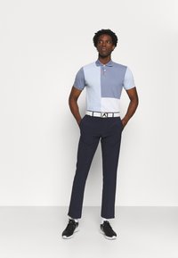 Short-sleeve polo shirt with blue tones and a color-block design, paired with navy pants. Complements with a white belt and black sneakers.