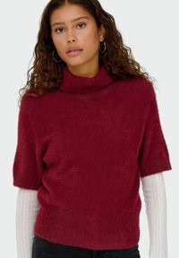 Burgundijska, kratkoslana turtleneck pulover od meke, teksturirane tkanine, s opuštenim krojem i rebrastim detaljima na izrezu.