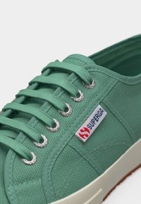 Πράσινο πάνινο αθλητικό παπούτσι με ταιριαστές κορδόνια, μεταλλικά ροδέλες, λευκή λαστιχένια σόλα και μικρή ετικέτα με το λογότυπο Superga στο πλάι.