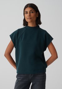 Pull à manches courtes couleur vert foncé avec un col ras du cou haut, en tissu lisse. Présente une coupe décontractée et un design global simple.