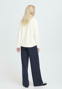 Bluză cu mânecă lungă, de culoare crem, combinată cu pantaloni largi de culoare bleumarin închis. Ansamblul are o croială relaxată și detalii minime.
