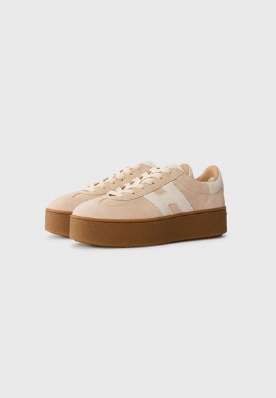 Beige suède sneakers met een dikke bruine rubberen zool, met een eenvoudig ontwerp en witte zijaccenten, vetersluiting.