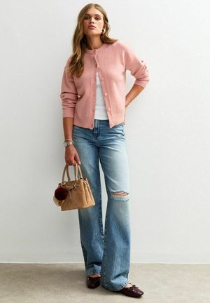 Lichtroze cardigan met knopen, witte top, versleten lichtblauwe jeans, bruine flats en een kleine tan handtas met een pompon-detail.
