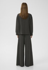 Set di abbigliamento da casa grigio scuro composto da una felpa dal taglio morbido e pantaloni a gamba larga realizzati in un tessuto morbido con una leggera texture.